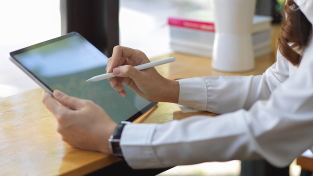 Vista lateral de las manos femeninas con simulacro de tableta digital en la barra de madera en la cafetería