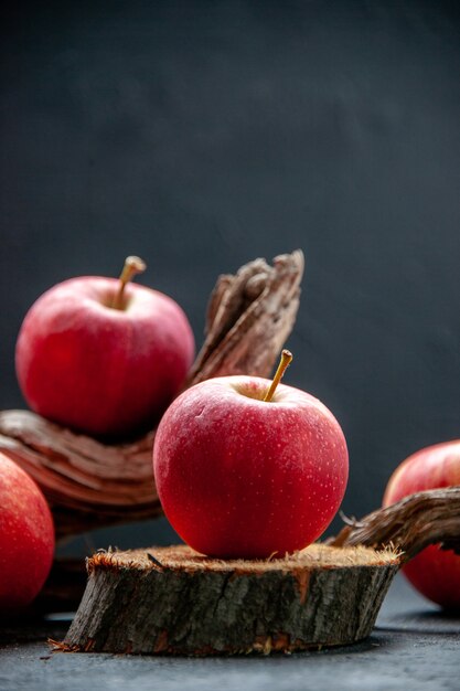 Vista lateral de manzanas frescas sobre tabla de cortar de madera y rama de árbol sobre fondo oscuro de la onda