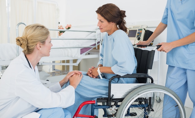 Vista lateral de un médico hablando con un paciente femenino en silla de ruedas en el hospital