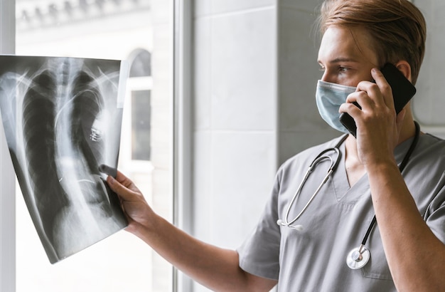 Foto vista lateral del médico mirando radiografía y hablando por teléfono