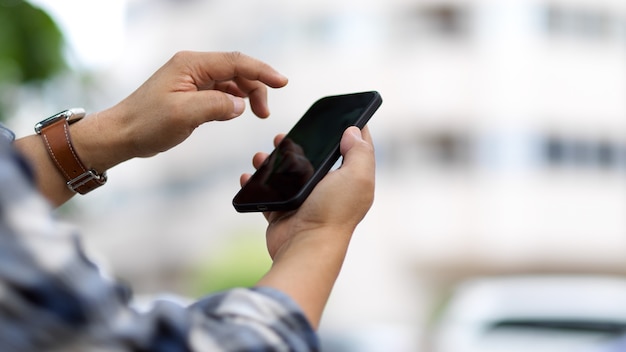 Vista lateral del mensaje de texto de manos masculinas en el teléfono inteligente mientras está de pie al aire libre