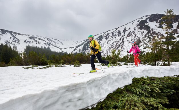 Vista lateral de mochileros esquiadores de fondo caminando sobre esquí en montañas boscosas Montaña cubierta de nieve en plena altitud