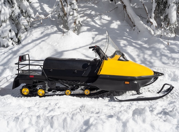 Vista lateral de la moto de nieve amarilla sobre la nieve en un día soleado de invierno