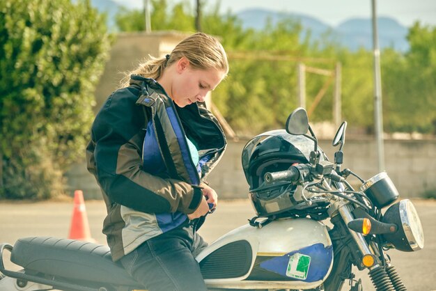 Vista lateral de una motociclista seria sentada en una motocicleta contemporánea y vistiendo una chaqueta en el motordromo