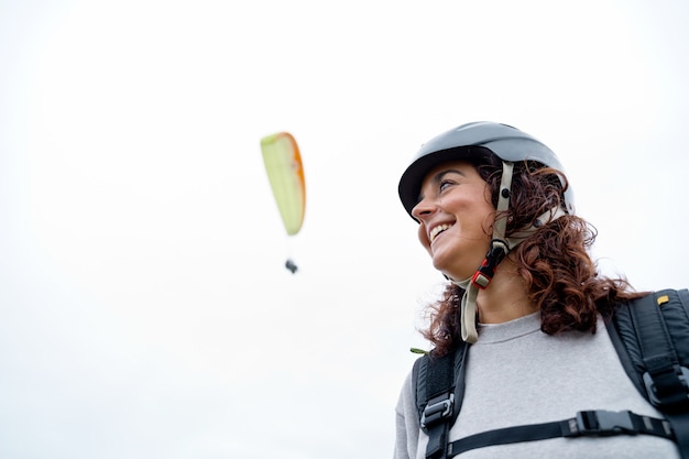 Foto vista lateral de la mujer alegre con casco y equipo de parapente al aire libre. vista panorámica de mujer aventurera practicando deportes de riesgo. estilo de vida de aventura y deporte.