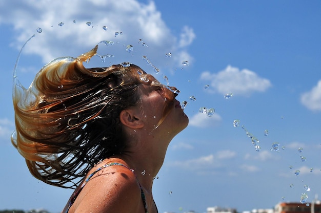 Foto vista lateral de una mujer arrojando el cabello mojado contra el cielo