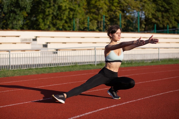 Vista lateral de una mujer atlética que viste ropa deportiva se calienta antes del entrenamiento cardiovascular en la mañana