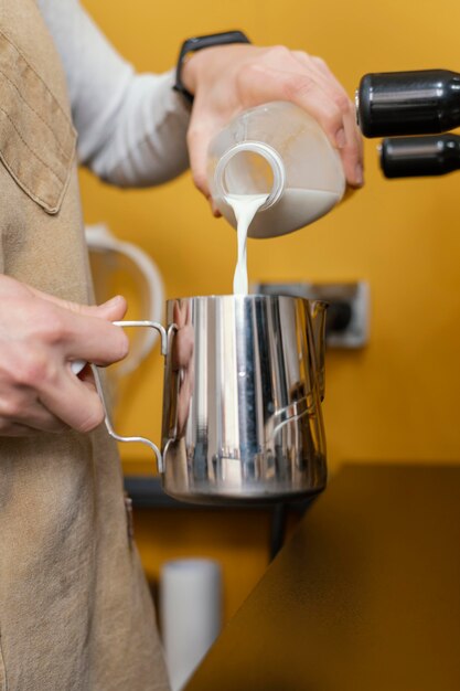 Foto vista lateral de la mujer barista vertiendo leche en taza