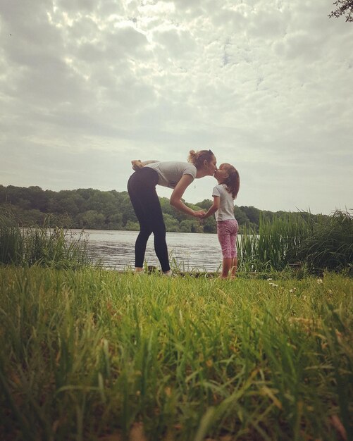 Foto vista lateral de una mujer besando a su hija en la orilla del lago