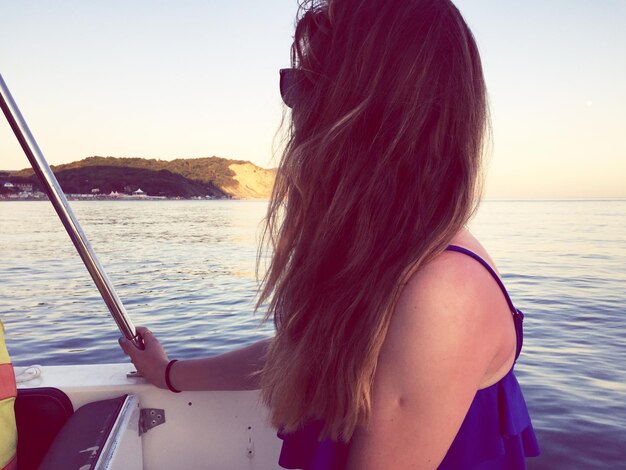 Foto vista lateral de una mujer de cabello largo sentada en un barco en el mar