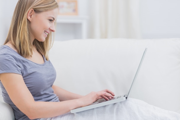 Vista lateral de la mujer casual usando la computadora portátil en el sofá