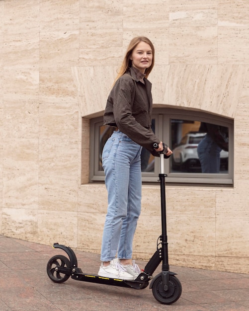 Foto vista lateral de la mujer en la ciudad en scooter eléctrico