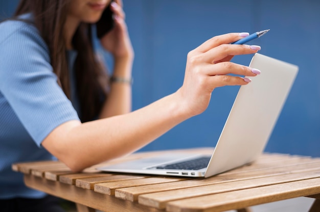 Foto vista lateral de la mujer desenfocada que trabaja en la computadora portátil mientras habla por teléfono inteligente