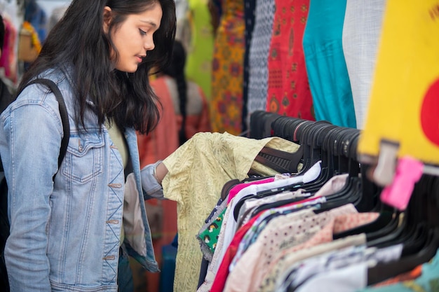 Foto vista lateral de una mujer eligiendo ropa en el mercado