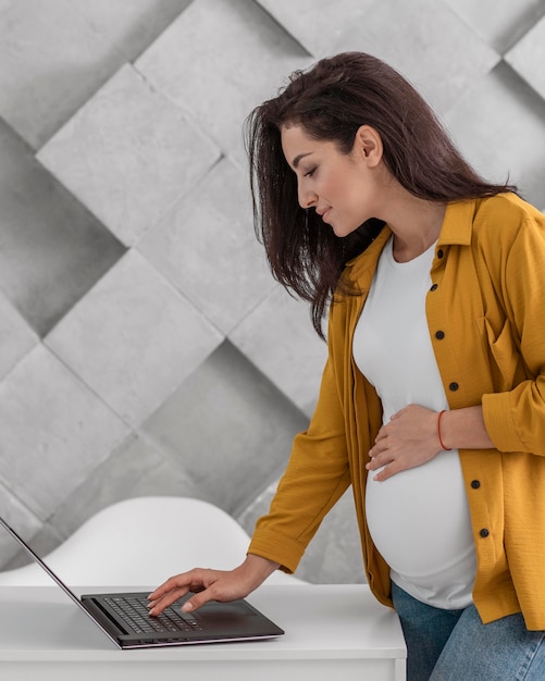 Foto vista lateral de la mujer embarazada que trabaja con el portátil en casa