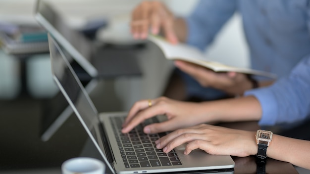 Vista lateral de una mujer escribiendo en la computadora portátil mientras su compañero de trabajo informa sobre su proyecto