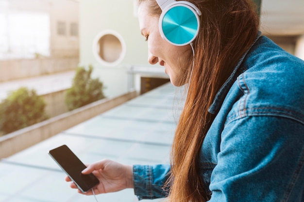 Foto vista lateral de la mujer escuchando música con auriculares mientras usa el teléfono inteligente
