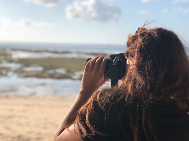 Foto vista lateral de una mujer fotografiando el mar contra el cielo