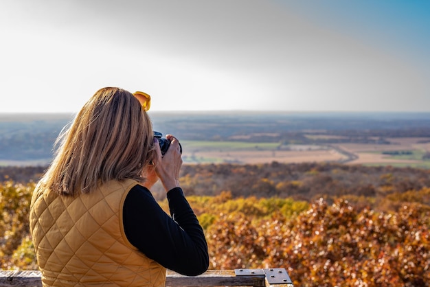 Foto vista lateral de una mujer fotografiando un paisaje con una cámara