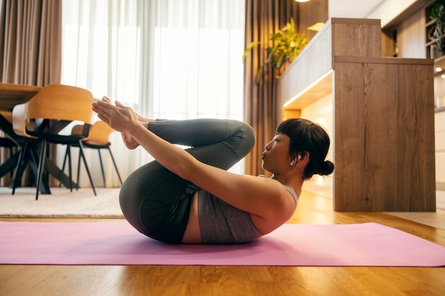 Vista lateral de una mujer japonesa de mediana edad practicando ejercicios de fitness y pilates en casa.