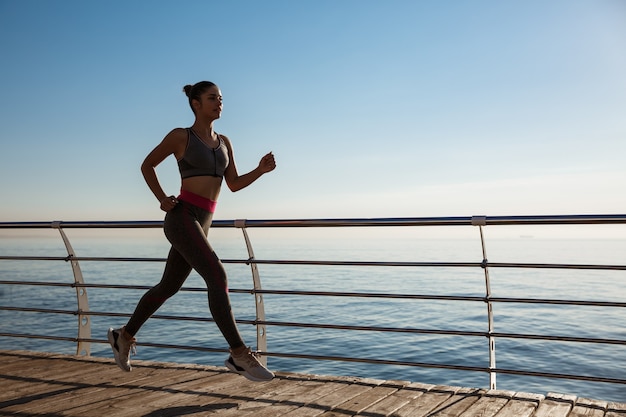 Vista lateral de la mujer joven fitness a lo largo del muelle.