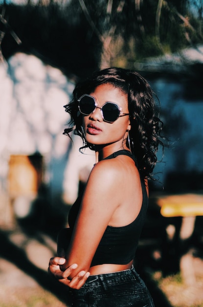 Foto vista lateral de una mujer joven con gafas de sol de pie al aire libre