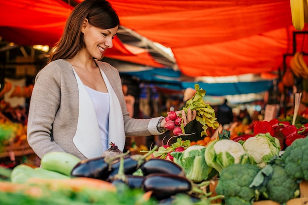 Foto vista lateral de la mujer joven en el mercado de los granjeros, eligiendo verduras.