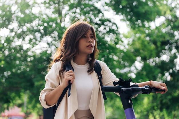 Foto vista lateral de una mujer joven con mochila montando scooter eléctrico en el parque