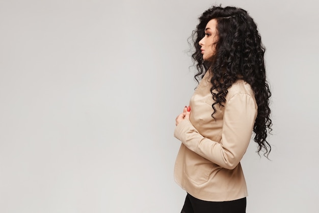 Vista lateral de la mujer joven modelo con pelo negro rizado en el fondo gris, aislado con espacio de copia a la izquierda.