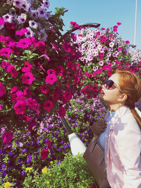 Foto vista lateral de una mujer joven oliendo flores rosadas en un día soleado