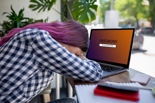 Vista lateral de una mujer joven de pelo rosa sentada en la mano de café escribiendo computadora portátil con contraseña de inicio de sesión ...