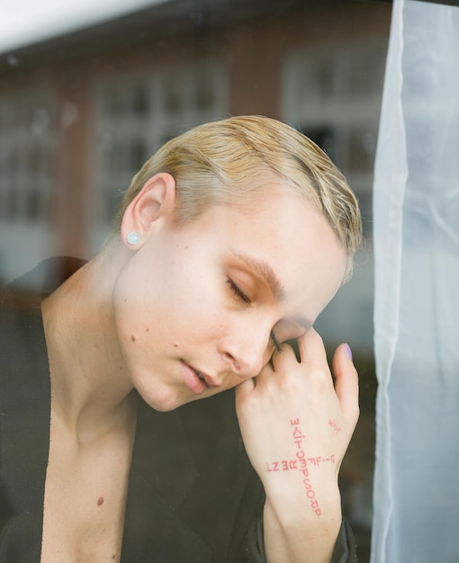 Foto vista lateral de una mujer joven de pie detrás de una ventana