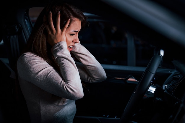 Vista lateral de la mujer joven que gesticula dentro del nuevo automóvil moderno.