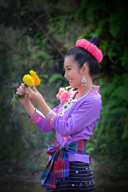 Foto vista lateral de una mujer joven con ropa tradicional sosteniendo flores mientras está de pie al aire libre