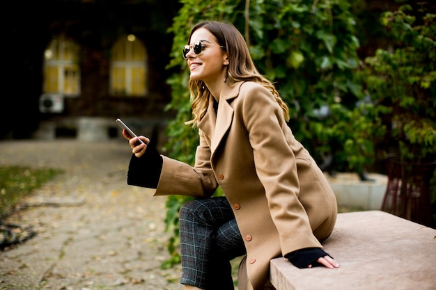 Vista lateral a la mujer joven sentada al aire libre y con teléfono móvil