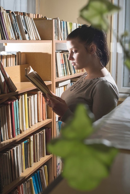 Foto vista lateral de una mujer leyendo un libro en una estantería de la biblioteca