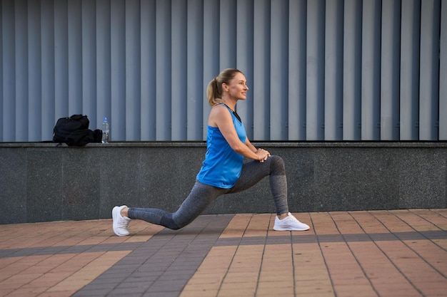 Vista lateral de una mujer madura deportiva en ropa deportiva mirando hacia otro lado mientras se calienta al aire libre