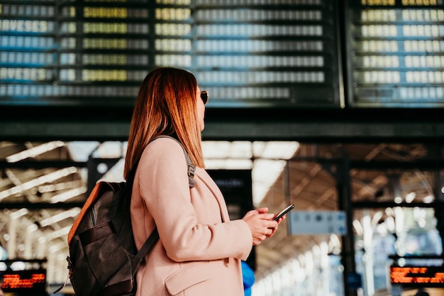 Vista lateral de una mujer con mochila de pie en la estación de tren