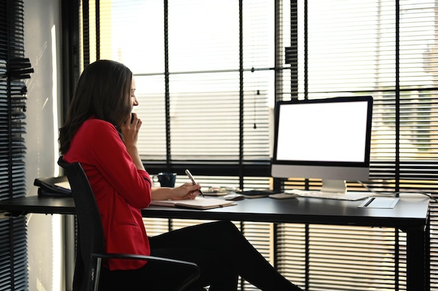 Vista lateral de una mujer de negocios caucásica leyendo información en línea en la pantalla de la computadora trabajando en una oficina moderna