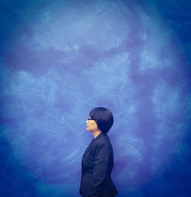 Vista lateral de una mujer de negocios de pie contra una pared azul