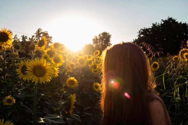 Vista lateral de una mujer de pie en una granja de girasoles contra un cielo despejado