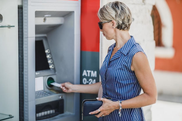 Vista lateral de una mujer que inserta una tarjeta de crédito y retira efectivo en un cajero automático.