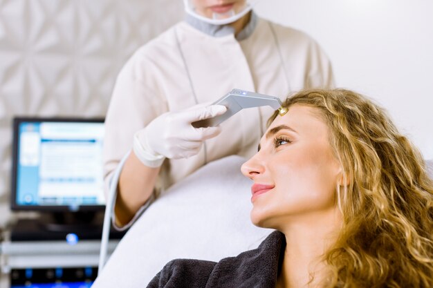 Vista lateral de la mujer rubia joven que recibe el masaje - microdermabrasion en clínica cosmetológica moderna. Exfoliación mecánica, pulido de diamantes.