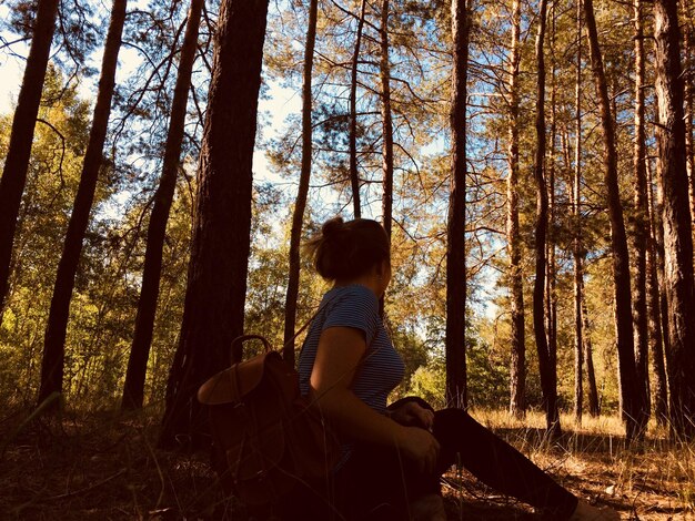 Foto vista lateral de una mujer sentada en tierra contra los árboles en el bosque