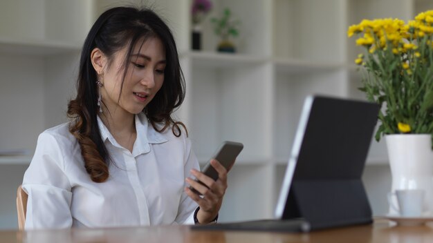 Vista lateral de la mujer con smartphone para relajarse mientras trabaja con tableta digital en la sala de la oficina