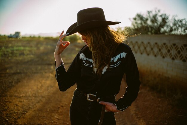 Foto vista lateral de una mujer con sombrero de vaquero y camisa occidental en la hora dorada