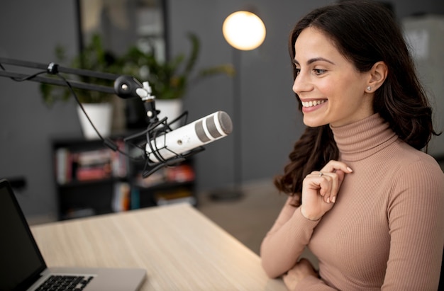 Foto vista lateral de la mujer sonriente en un estudio de radio con micrófono y portátil