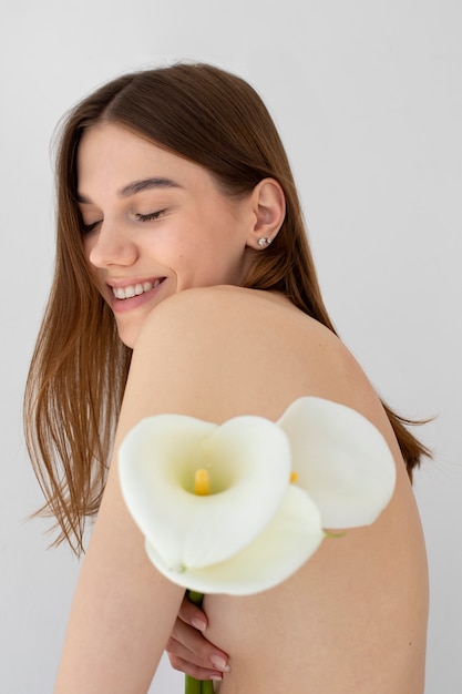 Vista lateral mujer sonriente posando desnuda con flores
