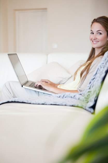 Vista lateral de la mujer sonriente con su laptop sentada en el sofá