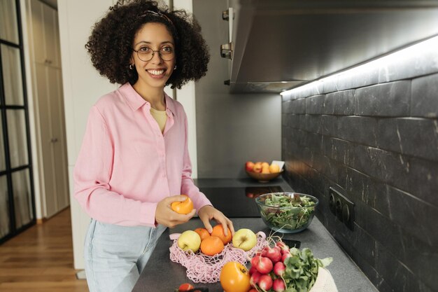 Vista lateral de la mujer de sonrisa negra cocinando y mirando a la cámara